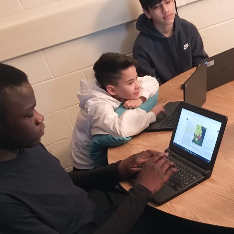 3 students sitting at a table working on laptops